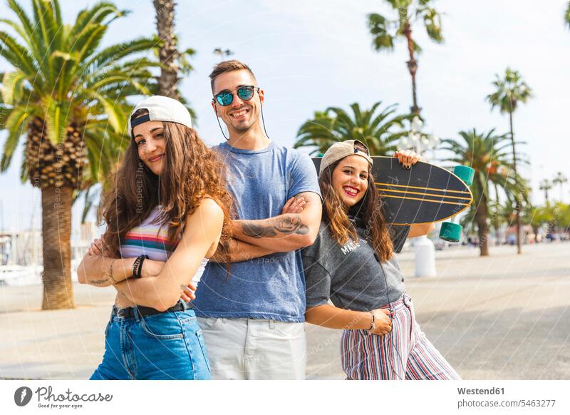 Drei glückliche Freunde posieren mit Skateboard auf einer Promenade mit Palmen Pose Promenaden Portrait Porträts Portraits Glück glücklich sein glücklichsein