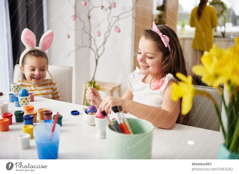 Schwestern sitzen am Tisch und bemalen Ostereier sitzend sitzt Ostern Osterfest glücklich Glück glücklich sein glücklichsein anmalen Mädchen weiblich Tische Ei