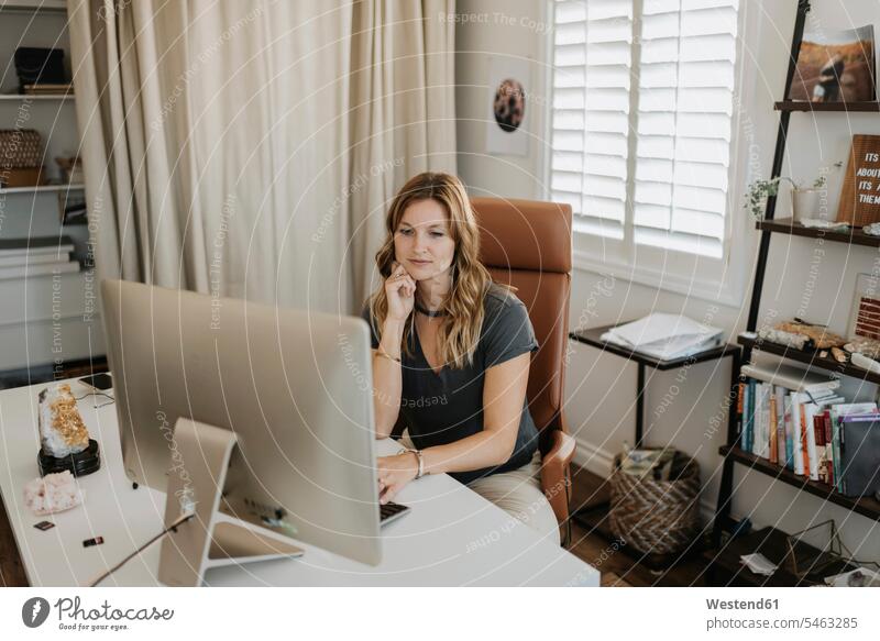 Mittlere erwachsene Frau, die zu Hause einen Computer am Schreibtisch benutzt Farbaufnahme Farbe Farbfoto Farbphoto Freizeitkleidung Freizeitbekleidung casual