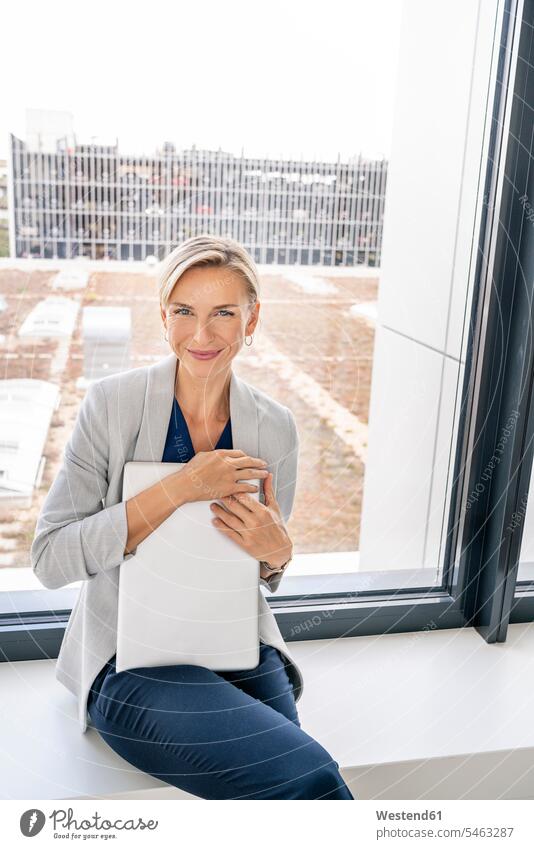 Blonde Geschäftsfrau mit Laptop, auf der Fensterbank eines Bürogebäudes sitzend Leute Menschen People Person Personen Europäisch Kaukasier kaukasisch 1 Ein