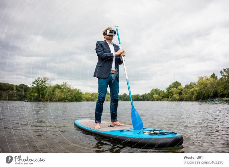 Geschäftsmann mit VR-Brille auf einem SUP-Brett auf einem See geschäftlich Geschäftsleben Geschäftswelt Geschäftsperson Geschäftspersonen Businessmann