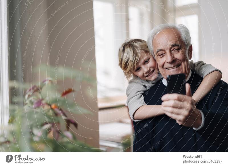 Glücklicher Großvater und Enkel telefonieren zu Hause Generation Telekommunikation Handies Handys Mobiltelefon Mobiltelefone Arm umlegen Umarmung Umarmungen