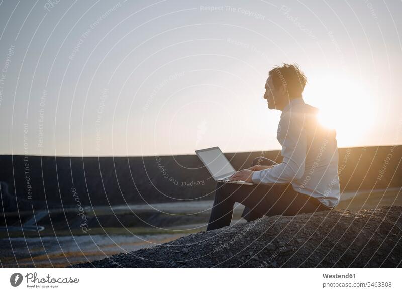 Reifer Geschäftsmann benutzt Laptop auf einer stillgelegten Minenhalde bei Sonnenuntergang Leute Menschen People Person Personen Europäisch Kaukasier kaukasisch