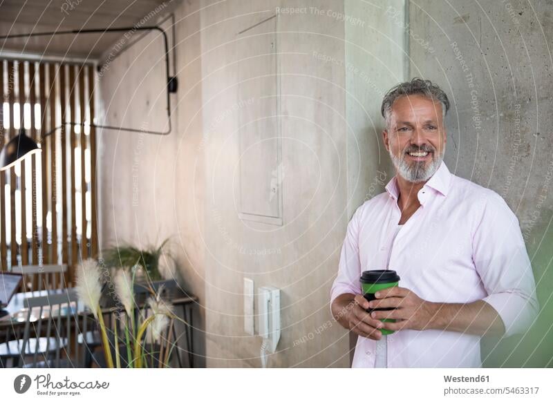 Lächelnder Geschäftsmann hält Kaffeebecher an Betonwand in einem Loft lächeln Betonwände Betonwaende Lofts Becher halten Businessmann Businessmänner