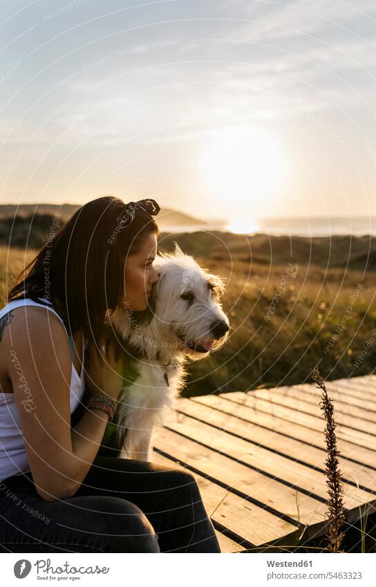 Frau kuschelt mit Hund auf einer Strandpromenade in den Dünen Tiere Tierwelt Haustiere Hunde entspannen relaxen sitzend sitzt sommerlich Sommerzeit