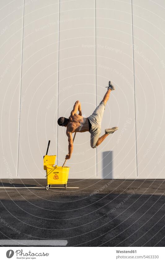 Acrobat spielt mit Putzeimer und Mopp Akrobat Akrobaten Eimer balancieren Balance springen hüpfen Trainieren Übung Üben Übungen Wischmopp ausgeglichen