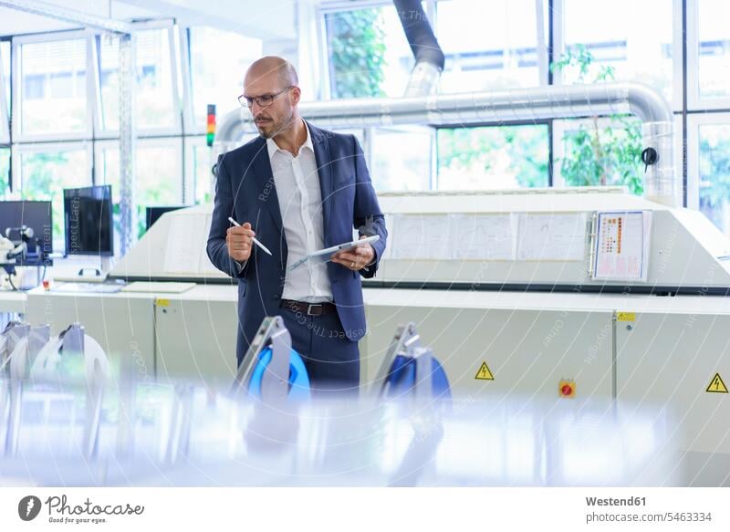 Ein reifer Mann hält ein digitales Tablett in der Hand, während er sich Maschinen in der Fabrik ansieht Farbaufnahme Farbe Farbfoto Farbphoto Innenaufnahme