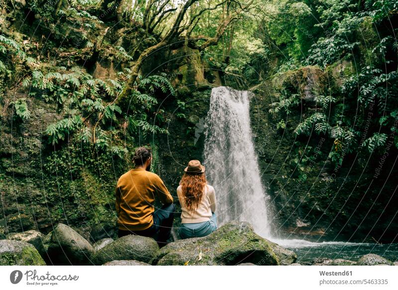 Rückansicht eines Paares, das an einem Wasserfall auf der Insel Sao Miguel, Azoren, Portugal Touristen sitzend sitzt geniessen Genuss erforschen Erforschung