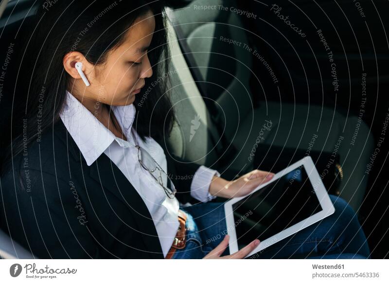 Junge Geschäftsfrau sitzt im Auto und benutzt Ohrstöpsel und digitales Tablet Leute Menschen People Person Personen erwachsen jung Millennial 18 - 19 Jahre