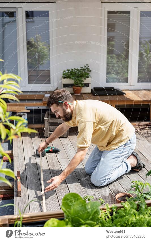Junger Handwerker baut Holzterrasse vor seinem Haus Messgerät Messinstrumente Meterstab Meterstäbe Zollstöcke DIY Do-it-Yourself Individuell Bauwerke Gebäude