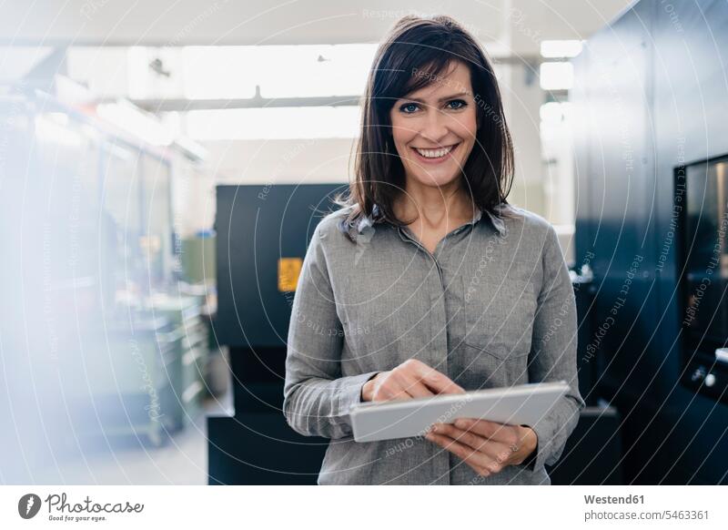 Porträt einer lächelnden Geschäftsfrau, die in einer Fabrik eine Tablette benutzt Job Berufe Berufstätigkeit Beschäftigung Jobs geschäftlich Geschäftsleben