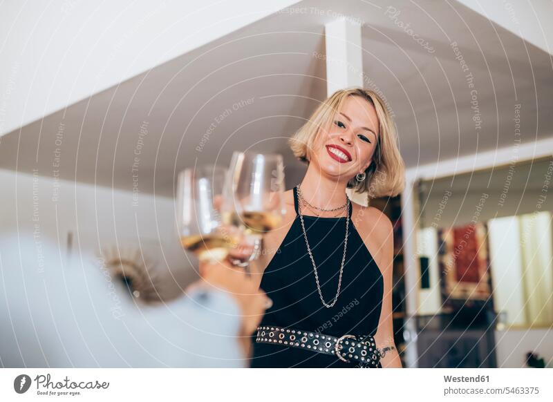 Lächelnde junge Frau stößt während der Party zu Hause auf Weingläser an Farbaufnahme Farbe Farbfoto Farbphoto Innenaufnahme Innenaufnahmen innen drinnen