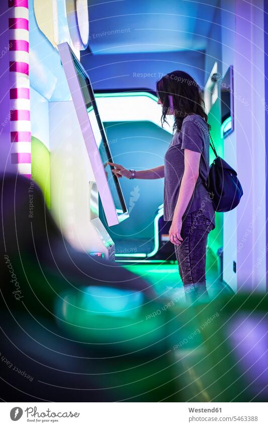Frau am Touchscreen in einer Spielhalle Rucksäcke T-Shirts Automat Spielautomaten Automaten Bildschirme Monitor Monitore Screen Screens stehend steht Muße