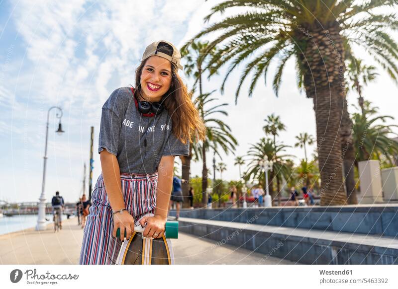 Porträt einer glücklichen Teenagerin mit Skateboard auf einer Promenade mit Palmen Portrait Porträts Portraits Promenaden Glück glücklich sein glücklichsein
