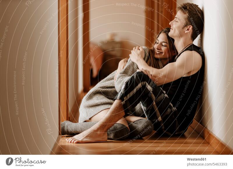 Glückliches junges Paar sitzt zu Hause auf dem Boden knuddeln schmusen sitzend Arm umlegen Umarmung Umarmungen entspannen relaxen entspanntheit relaxt freuen
