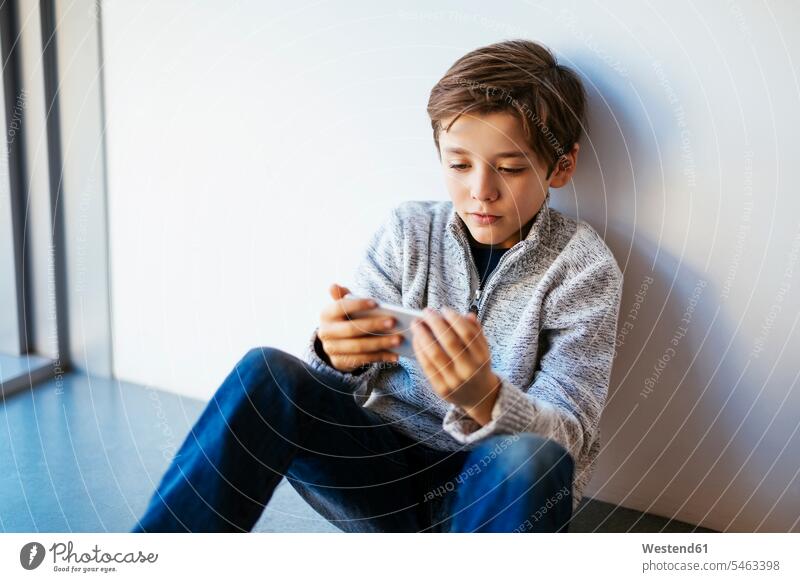 Junge sitzt auf dem Boden und schaut auf sein Handy Buben Knabe Jungen Knaben männlich Mobiltelefon Handies Handys Mobiltelefone Böden Boeden sitzen sitzend
