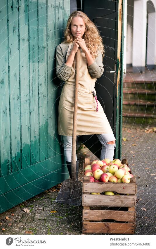 Porträt einer selbstbewussten Frau, die an einer Kiste mit Äpfeln steht stehen stehend Holzkiste Steige Holzverschlag weiblich Frauen Portrait Porträts