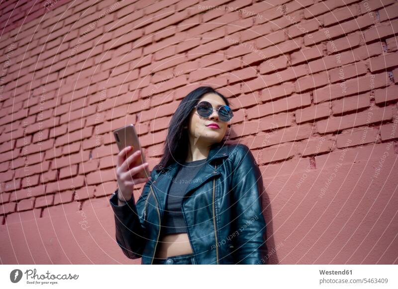 Porträt der jungen Frau mit Smartphone trägt Sonnenbrille und schwarze Lederjacke iPhone Smartphones Sonnenbrillen Brille schwarzer schwarzen schwarzes Portrait