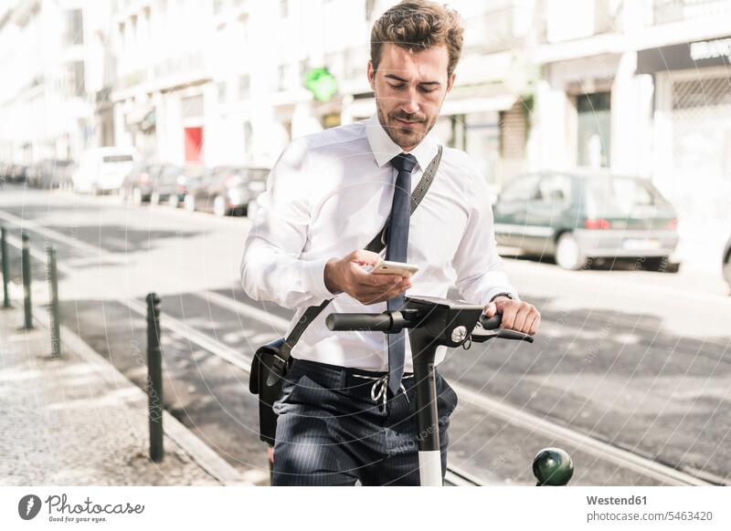 Junger Geschäftsmann mit einem E-Scooter, der ein Mobiltelefon in der Stadt benutzt, Lissabon, Portugal geschäftlich Geschäftsleben Geschäftswelt