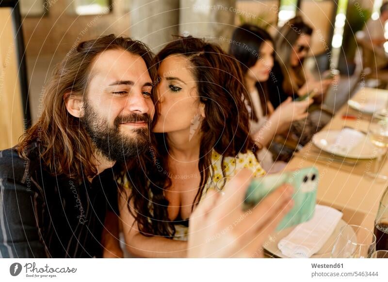Mann macht Selfie, während Frau ihn im Restaurant küsst Farbaufnahme Farbe Farbfoto Farbphoto Spanien Innenaufnahme Innenaufnahmen innen drinnen Tag