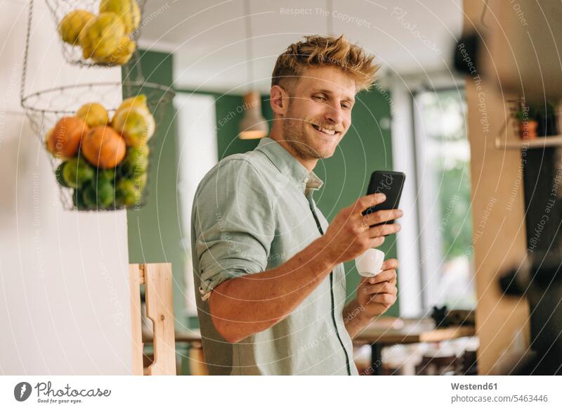Junger Geschäftsinhaber trinkt Kaffee, prüft Smartphone genießen geniessen Genuss trinken iPhone Smartphones SMS Textnachricht Cafe Kaffeehaus Bistro Cafes Café