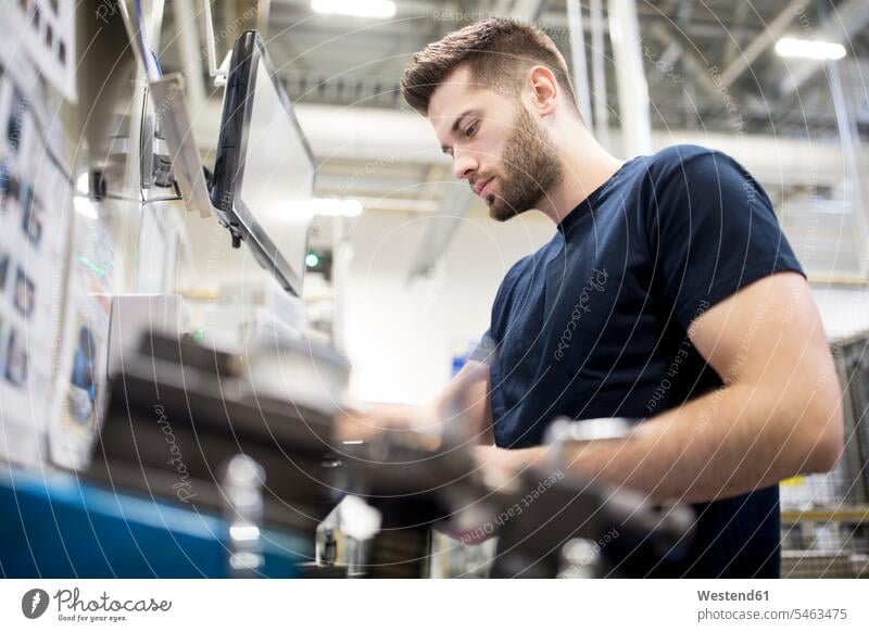 Mann, der in einer modernen Fabrik arbeitet und eine Maschine bedient Job Berufe Berufstätigkeit Beschäftigung Jobs Arbeiter T-Shirts Bildschirme Monitor