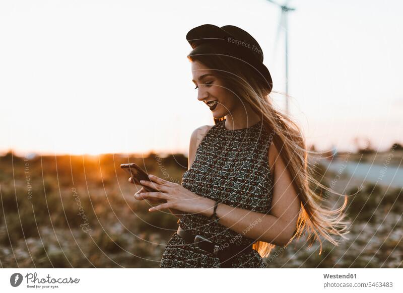 Porträt einer jungen Frau, die bei Sonnenuntergang auf ihr Handy schaut Portrait Porträts Portraits Sonnenuntergänge ansehen weiblich Frauen Smartphone iPhone
