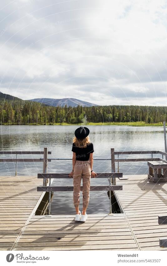Finnland, Lappland, Frau mit Hut auf einem Steg an einem See stehend Hüte Seen Stege Anlegestelle weiblich Frauen steht Gewässer Wasser Erwachsener erwachsen