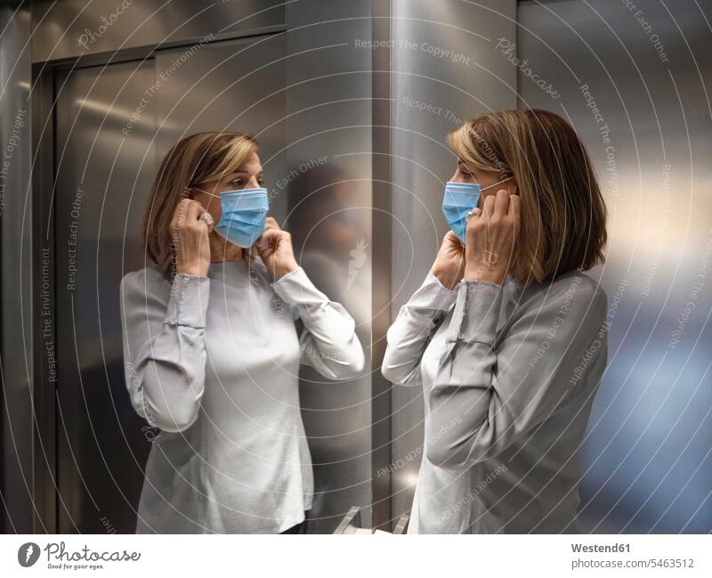Ältere Frau, die eine schützende Gesichtsmaske trägt, während sie im Aufzug steht, während Covid-19 Farbaufnahme Farbe Farbfoto Farbphoto Innenaufnahme