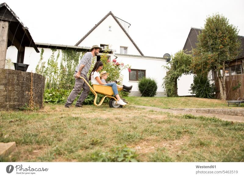 Playful Mann schiebt Frau und Sohn sitzen in Schubkarre im Garten Familie Familien sitzend sitzt Karre Karren Schubkarren Gärten Gaerten verspielt spielerisch