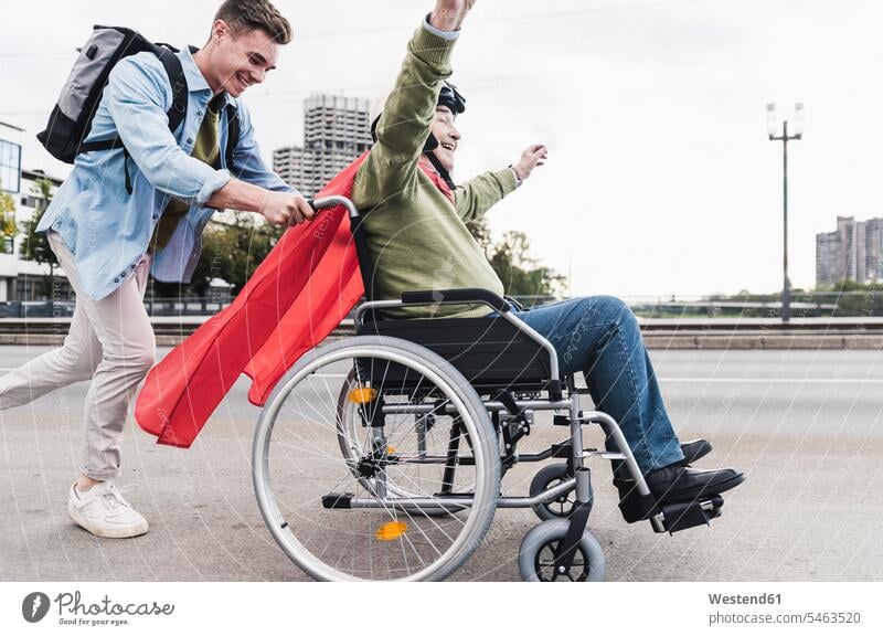Junger Mann schiebt älteren Mann, der als Superheld verkleidet in einem Rollstuhl sitzt Leute Menschen People Person Personen Europäisch Kaukasier kaukasisch 2