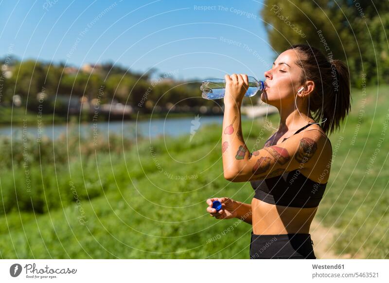 Sportliche junge Frau bei einer Abkühlungspause am Flussufer hoeren Jahreszeiten sommerlich Sommerzeit durstig entspannen relaxen entspanntheit relaxt Farben