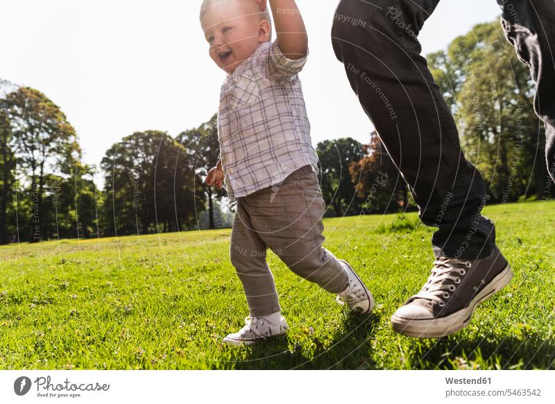 Vater geht Hand in Hand mit seinem Sohn in einem Park Söhne Parkanlagen Parks aktiv gehen gehend Papas Väter Vati Vatis Papis Kind Kinder Familie Familien