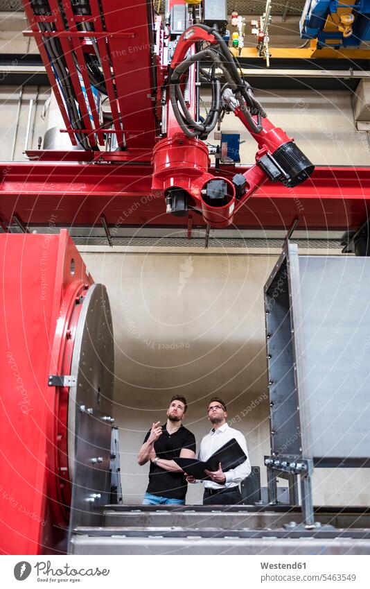 Zwei Männer mit Falzapparat betrachten Maschine in der Fabrikhalle Maschinen Produktionshalle Montagehalle Mappe Mappen Ordner Mann männlich ansehen Fabriken