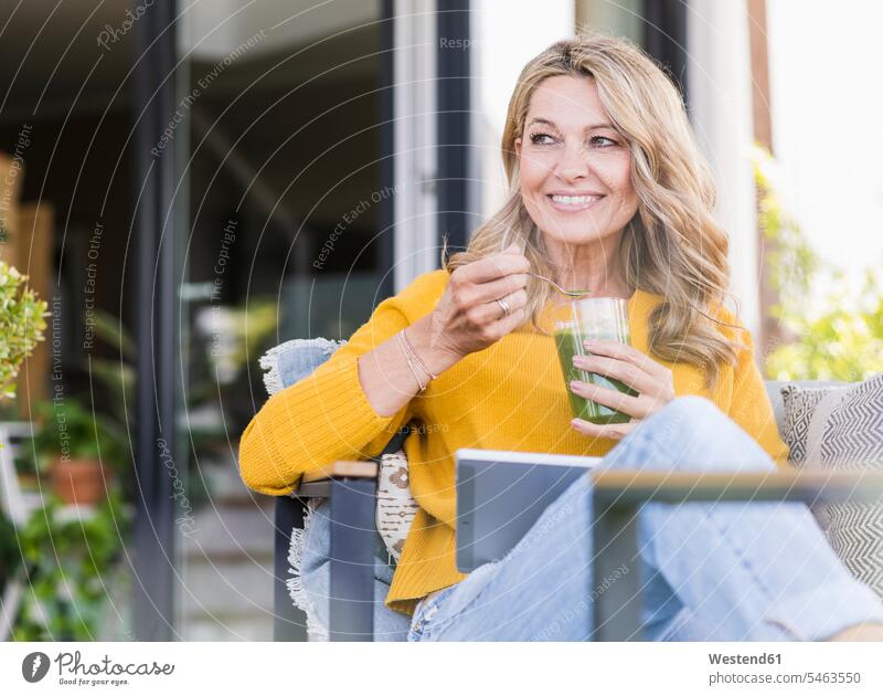 Porträt einer lächelnden reifen Frau, die mit einem digitalen Tablet auf der Terrasse sitzt und einen grünen Smoothie genießt Gläser Trinkglas Trinkgläser