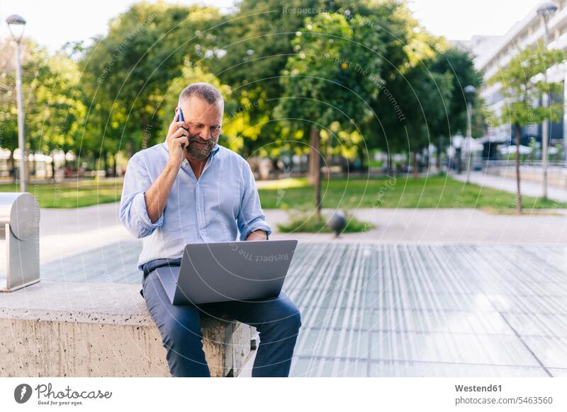 Geschäftsmann benutzt Laptop, während er im Büropark mit dem Handy telefoniert Geschäftsleute Geschäftsperson Geschäftspersonen Business Geschäftsleben