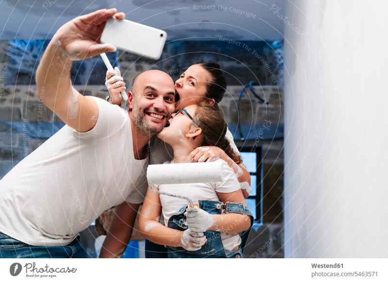 Glückliche Familie macht ein Selfie beim Streichen der Wände ihres neuen Hauses T-Shirts Telekommunikation telefonieren Handies Handys Mobiltelefon