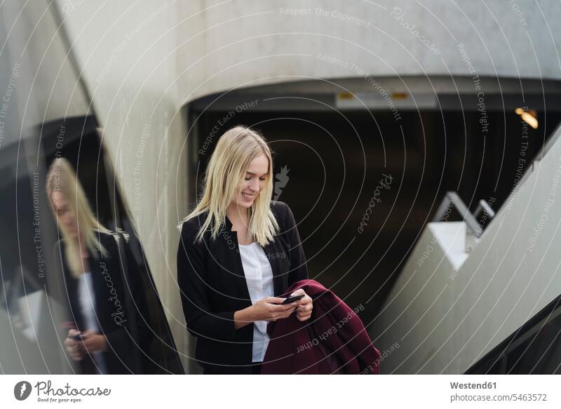 Blonde Geschäftsfrau benutzt Smartphone bei Benutzung der Rolltreppe Leute Menschen People Person Personen Europäisch Kaukasier kaukasisch 1 Ein ein Mensch eine
