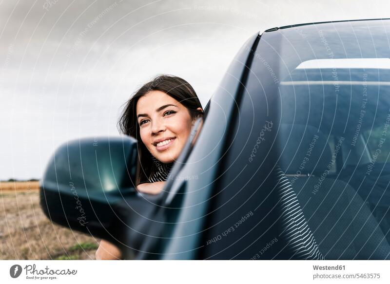 Lächelnde junge Frau lehnt sich aus dem Autofenster Fenster Wagen PKWs Automobil Autos lächeln weiblich Frauen glücklich Glück glücklich sein glücklichsein
