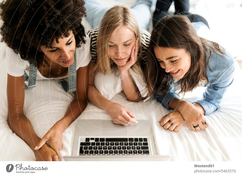 Drei Freundinnen liegen auf dem Bett und teilen sich einen Laptop liegend liegt Betten Notebook Laptops Notebooks Frau weiblich Frauen Teilen Sharing Freunde