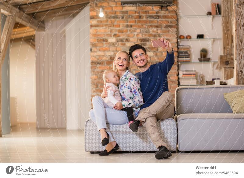 Glückliche junge Eltern machen ein Selfie auf der Couch zu Hause mit ihrem kleinen Mädchen Sofa Couches Liege Sofas glücklich glücklich sein glücklichsein