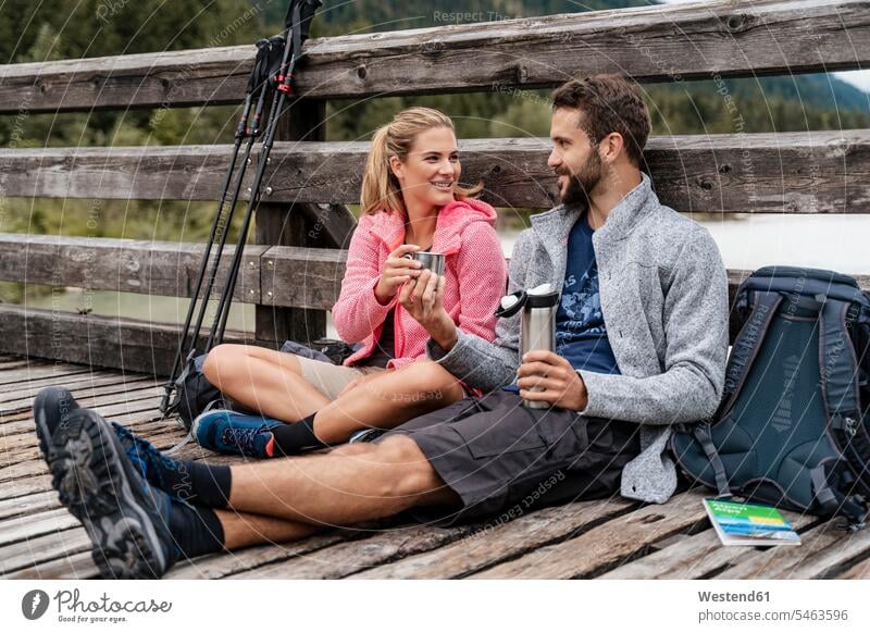 Junges Paar macht während einer Wanderung auf einer Holzbrücke eine Pause, Vorderriss, Bayern, Deutschland Touristen Rucksäcke Jacken überreichen gehend geht