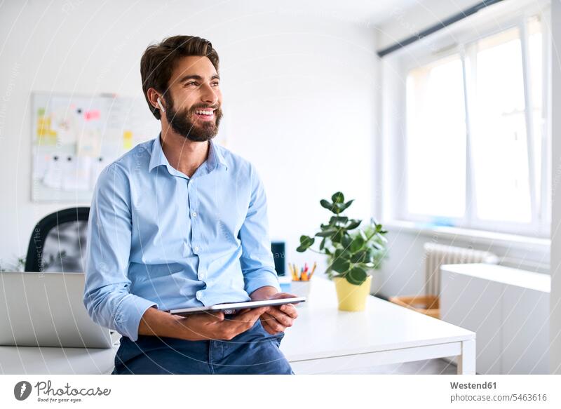 Lächelnder Geschäftsmann mit Kopfhörern, der ein digitales Tablet in seinem Büro benutzt Job Berufe Berufstätigkeit Beschäftigung Jobs Designer geschäftlich