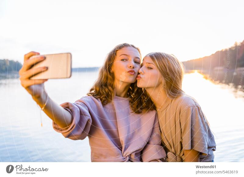 Freunde spitzen die Lippen, während sie mit dem Smartphone gegen den See fahren Farbaufnahme Farbe Farbfoto Farbphoto Außenaufnahme außen draußen im Freien