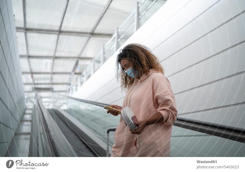 Junge Frau benutzt Smartphone, während sie auf der Rolltreppe am Flughafen steht Farbaufnahme Farbe Farbfoto Farbphoto Innenaufnahme Innenaufnahmen innen