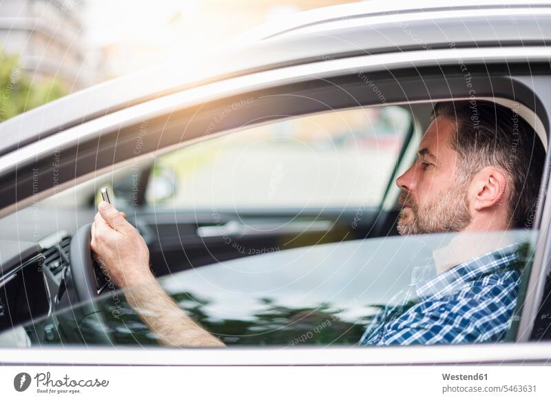 Seitenansicht eines gut aussehenden Mannes, der ein Mobiltelefon benutzt, während er im Auto sitzt Farbaufnahme Farbe Farbfoto Farbphoto Deutschland