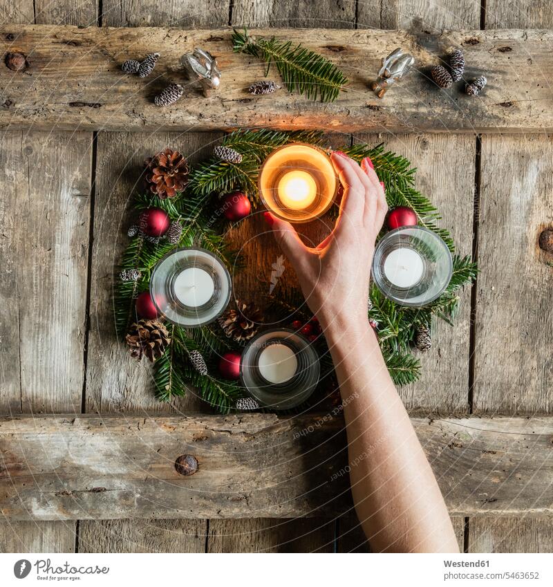 Hand einer Frau berührt Glasabdeckung einer Kerze, die auf dem Adventskranz brennt Innenaufnahme Innenaufnahmen innen drinnen Draufsicht von oben Aufsicht