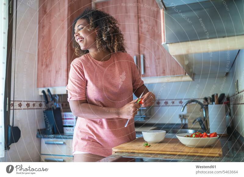 Fröhliche junge Frau schaut weg, während sie zu Hause auf der Küchentheke Erdbeeren schneidet Farbaufnahme Farbe Farbfoto Farbphoto Spanien