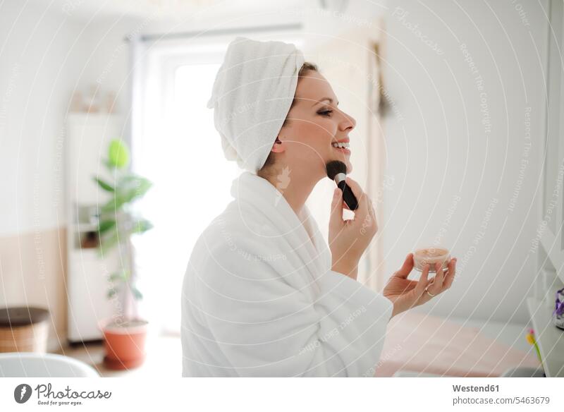 Lächelnde Frau im Bademantel beim Auftragen von Make-up am Morgen zu Hause lächeln Make up Schminke schminken anwenden auftragen Bademäntel weiblich Frauen