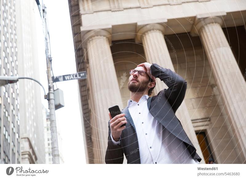 Porträt eines besorgten jungen Geschäftsmannes mit Handy vor der Börse, New York City, USA geschäftlich Geschäftsleben Geschäftswelt Geschäftsperson